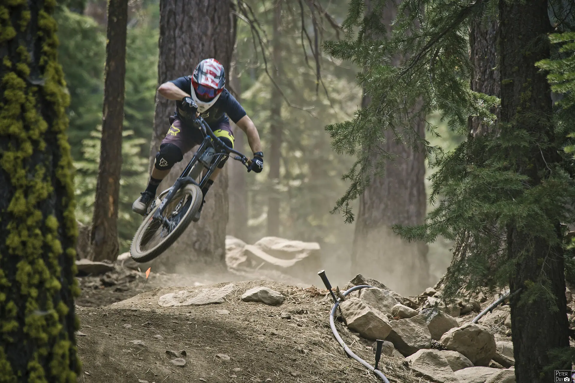 Downhill mountain biker railing a dusty berm through the trees