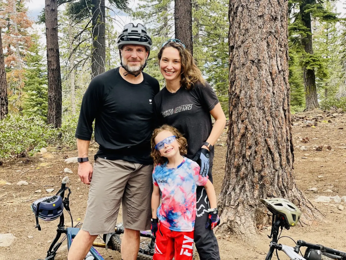 A family of three with mountain bikes under a pine tree