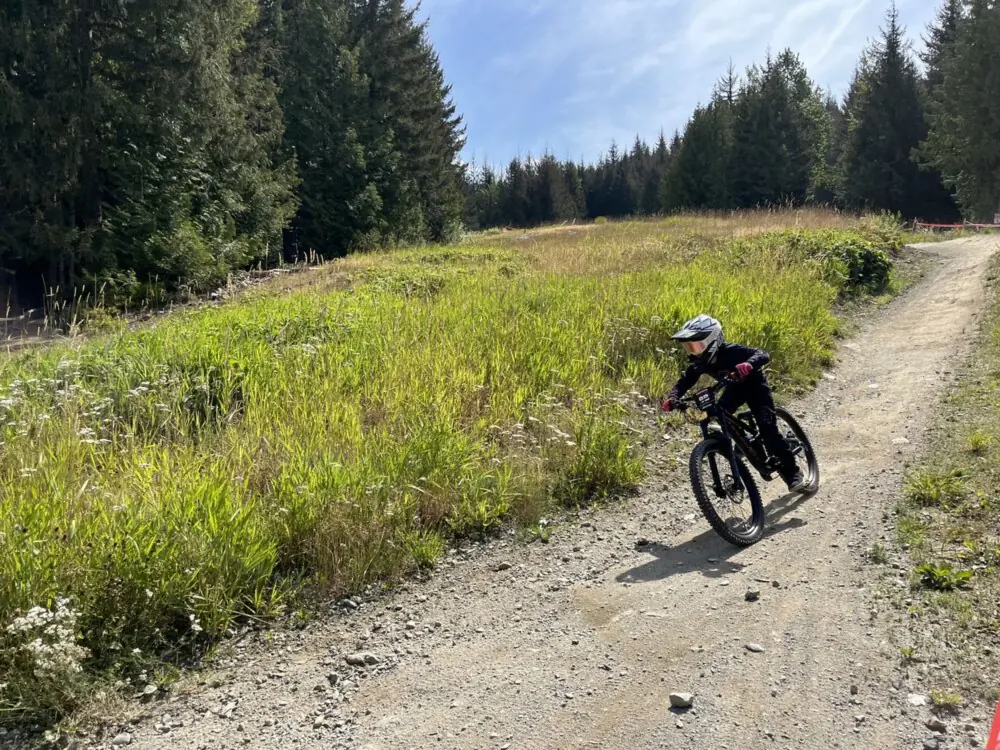 A kid riding a mountain bike up a gravel road through a meadow