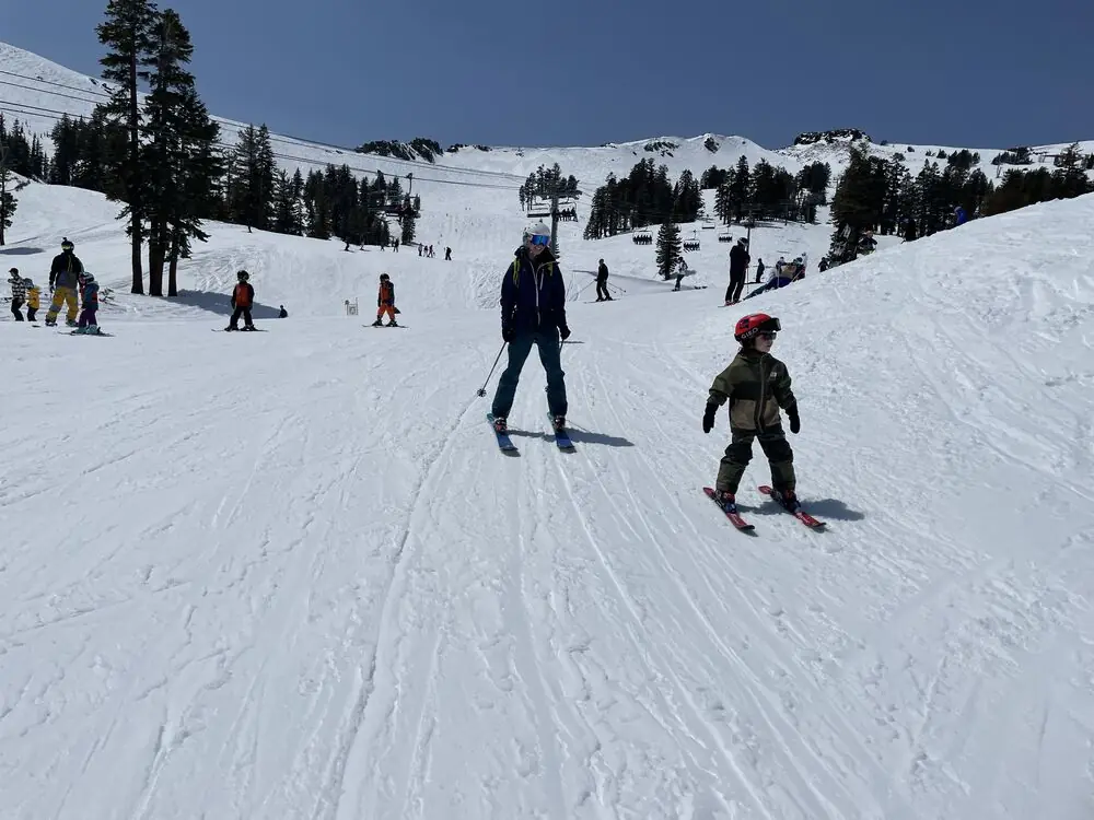 A parent skiing behind a small kid on a wide groomed run
